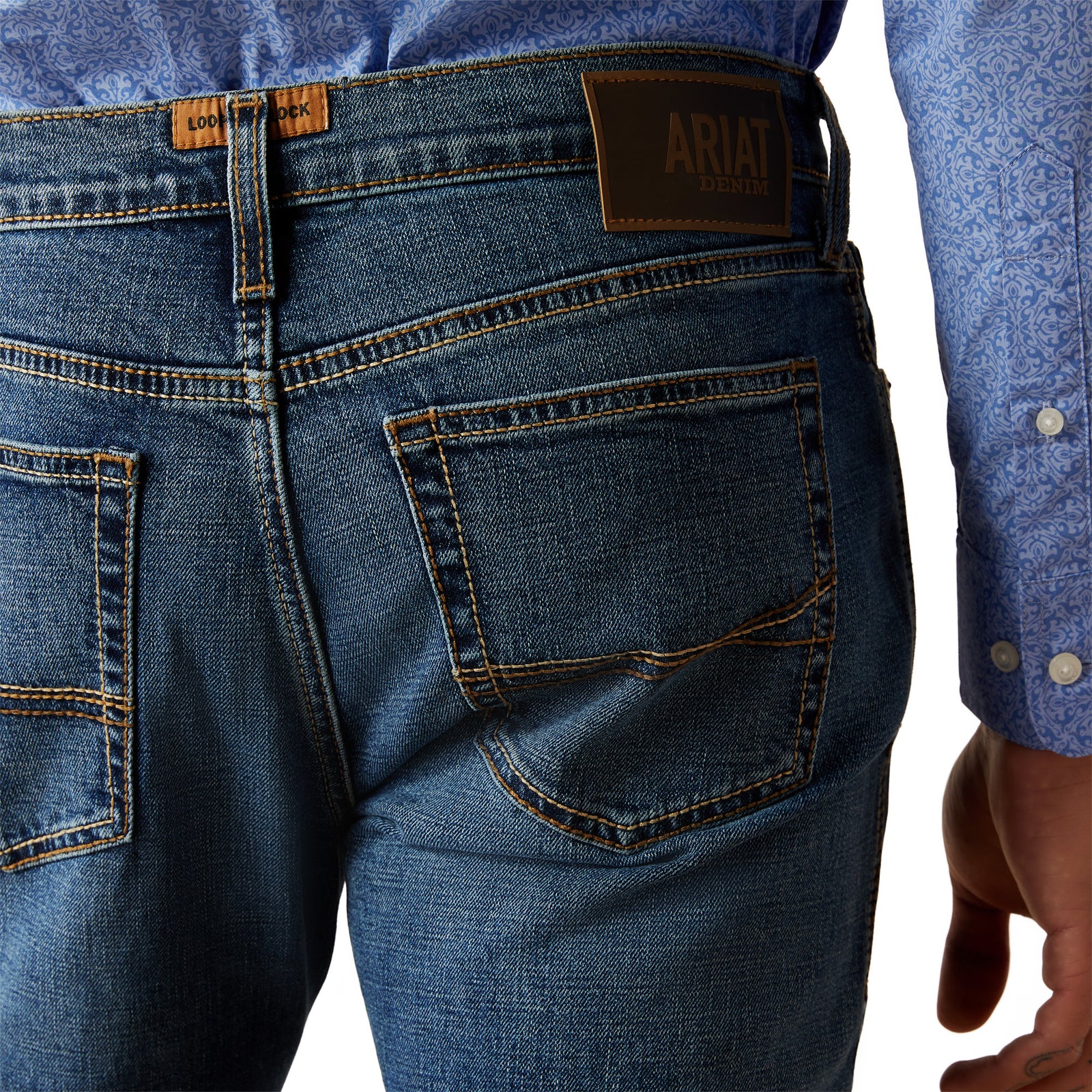 Ariat Men's M8 Miles Modern Fit Jean. Close-up of blue jeans with Ariat branding on a white background