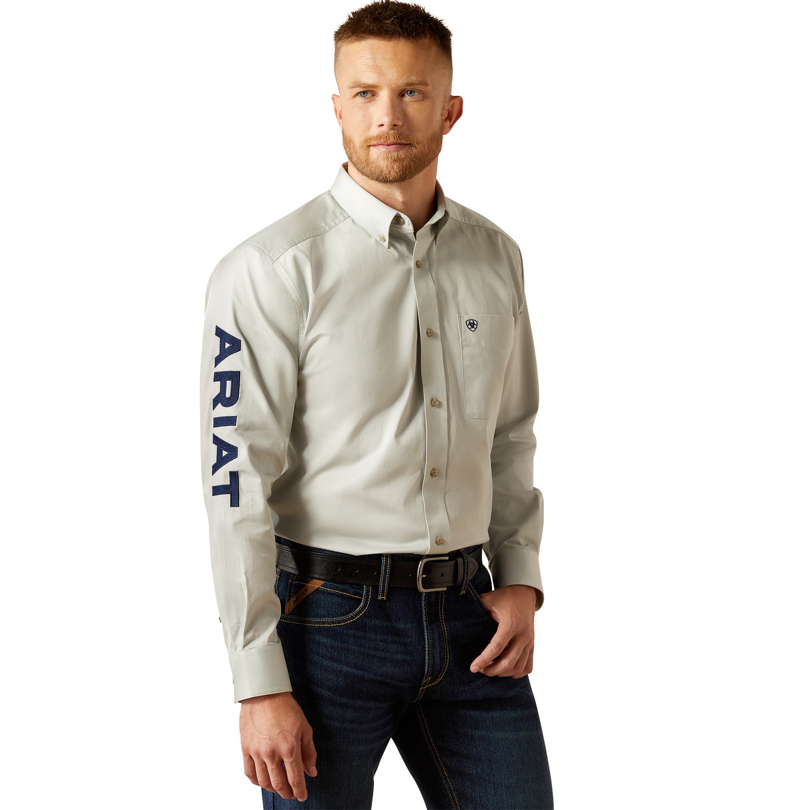 Ariat Men's Team Logo Twill L/S Western Shirt. Man wearing a light gray button-up shirt with 'Ariat' branding on a white background