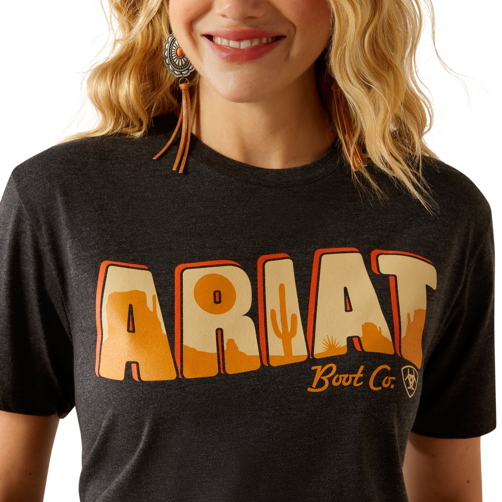 Ariat Women's Postcard T-Shirt. Person wearing a black t-shirt with 'Ariat Boot Co.' text and cactus graphic.
