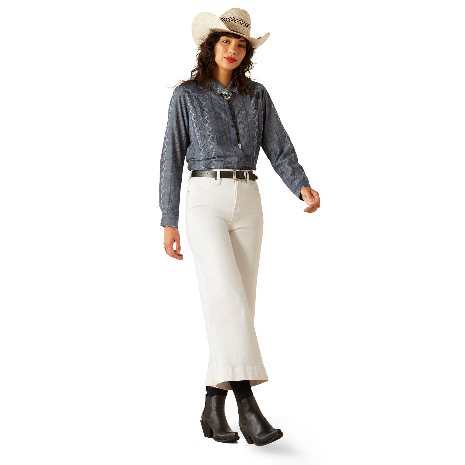 Ariat Women's Billie Jean L/S Western Shirt. Woman wearing a denim shirt, white pants, and a cowboy hat on a white background