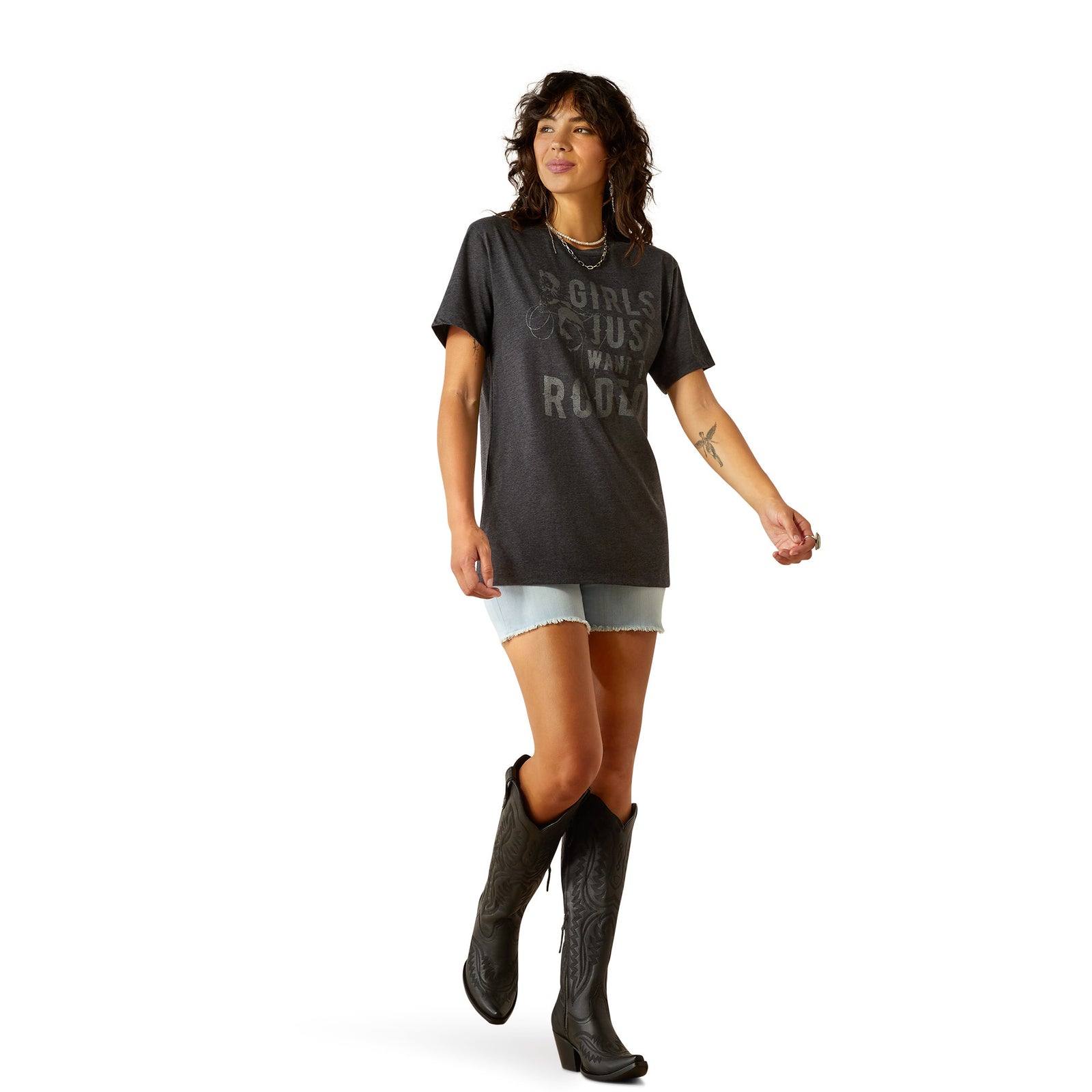 Àriat Women's Rodeo Girls T-Shirt. Woman wearing a dark gray t-shirt with text and light denim shorts, standing on a white background.