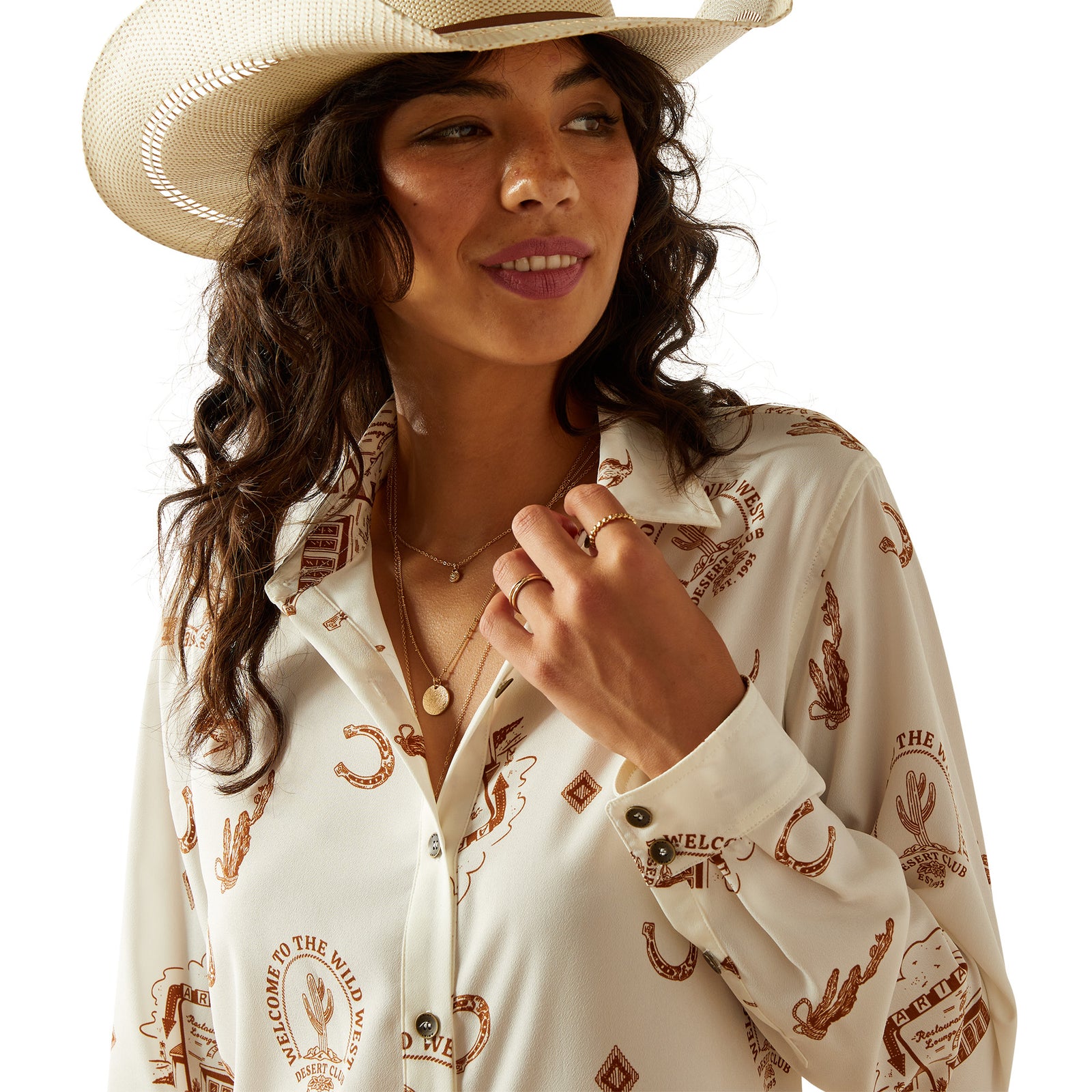 Ariat Women's Homestyle Button Up L/S Western Shirt. Woman wearing a white cowboy shirt with brown patterns and a beige cowboy hat on a white background