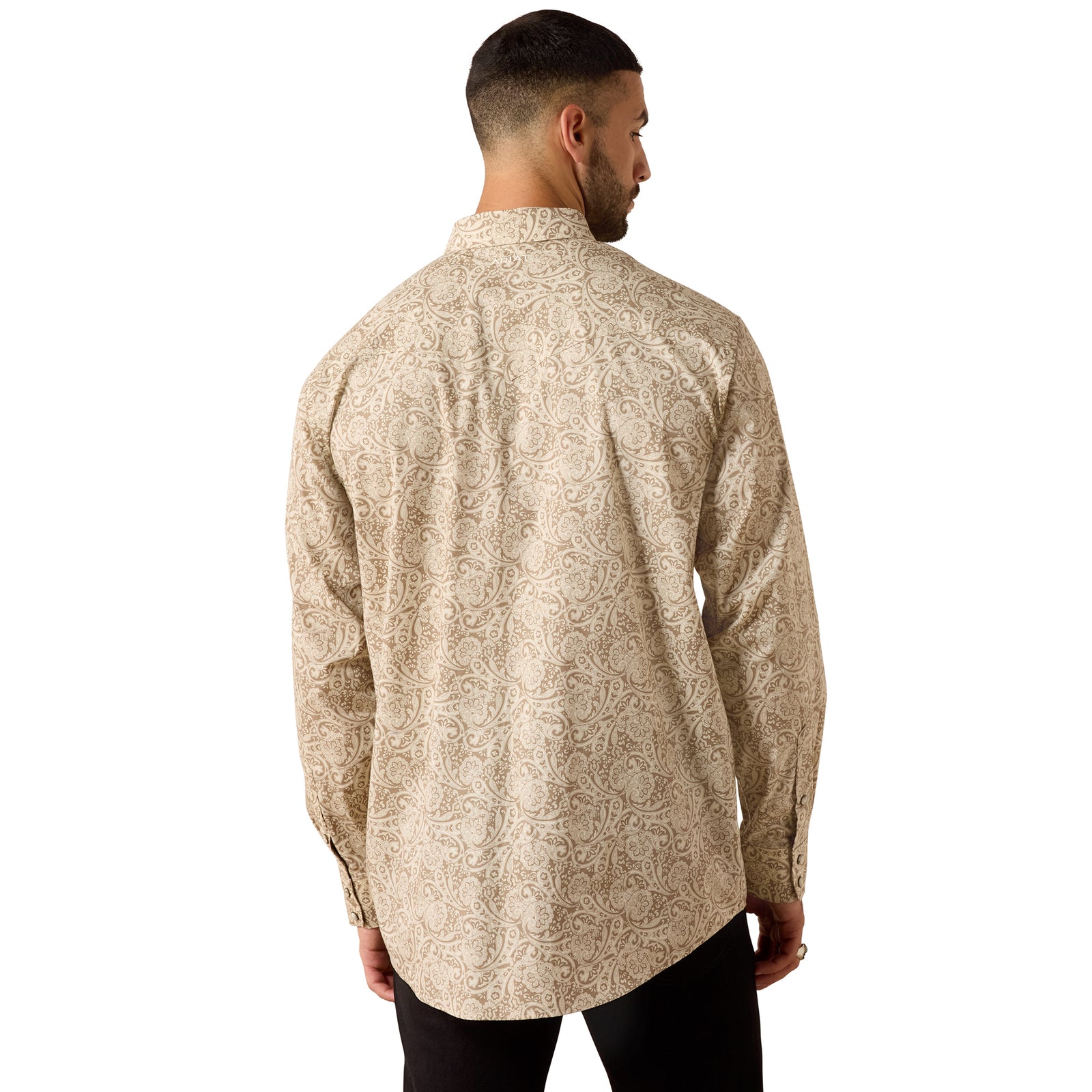 A man viewed from the back wearing a beige long-sleeve button-up shirt with a light brown floral paisley pattern, paired with black pants, against a plain white background.