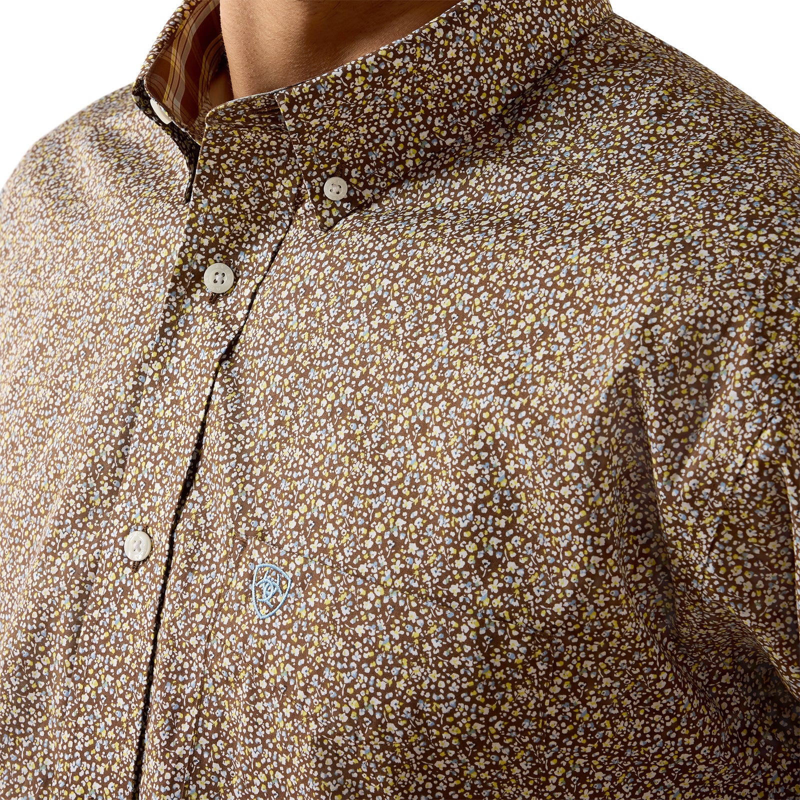 Close-up of a men's button-down shirt featuring a dense, small-scale floral or ditsy print in brown, beige, and white, worn by a model.