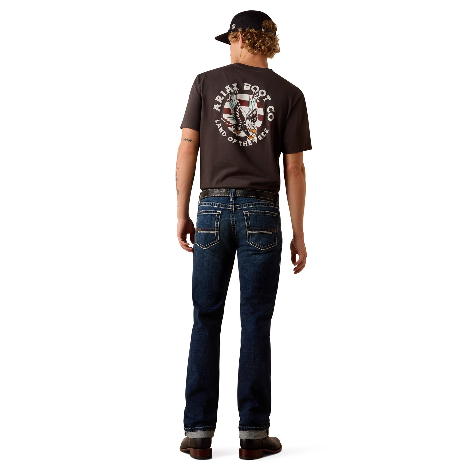 Man wearing a dark brown t-shirt with a graphic design on the back and blue jeans, standing against a white background.