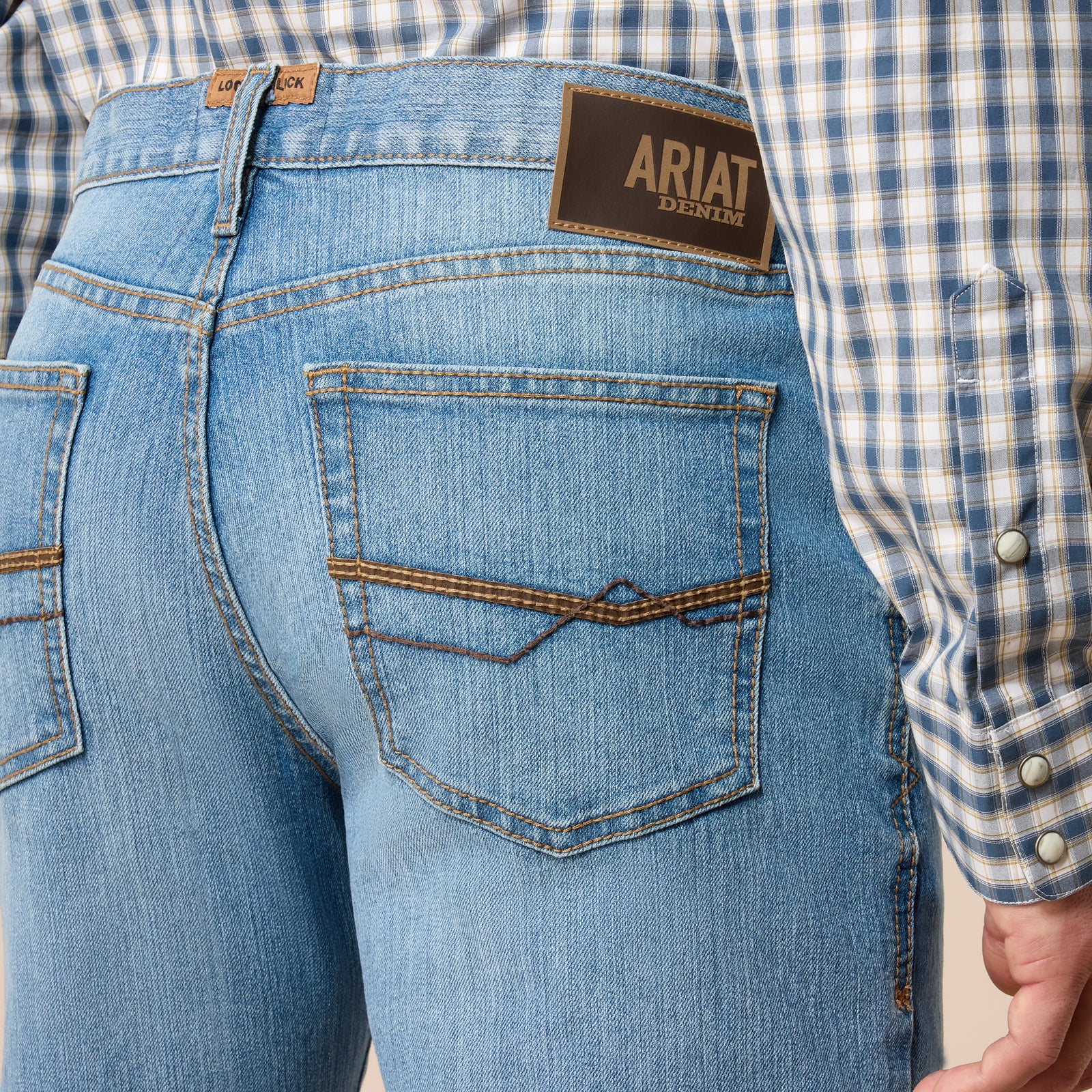 Close-up of blue jeans with Ariat logo, worn with a plaid shirt.