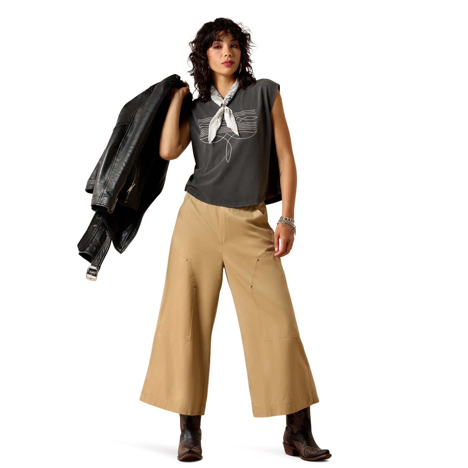 Woman wearing a gray top with a white bow, beige wide-leg pants, and holding a black jacket on a white background