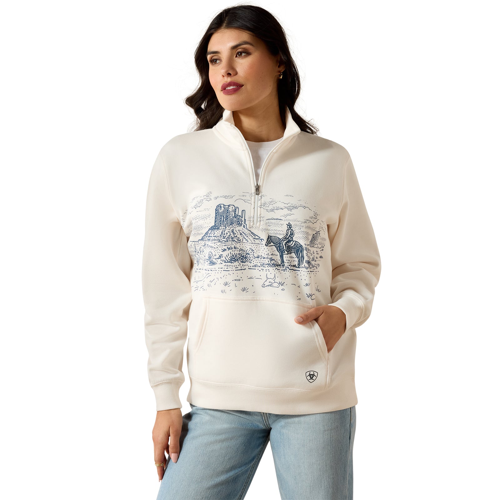 A woman modeling a cream-colored quarter-zip hoodie with a blue western landscape graphic on the front, paired with light blue jeans, against a plain white background.