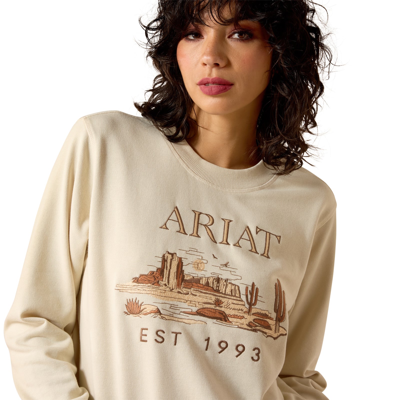 Woman wearing a beige Ariat sweatshirt with a graphic design on a white background