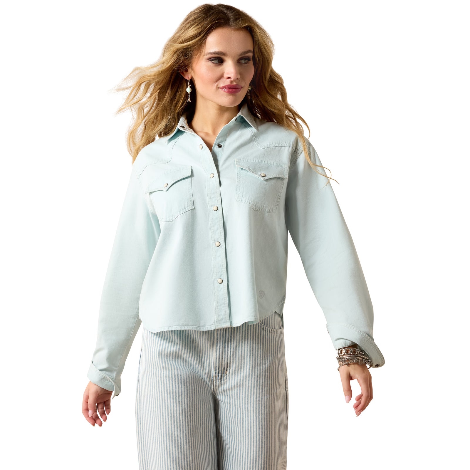 Woman wearing a light blue denim shirt and white pants on a white background