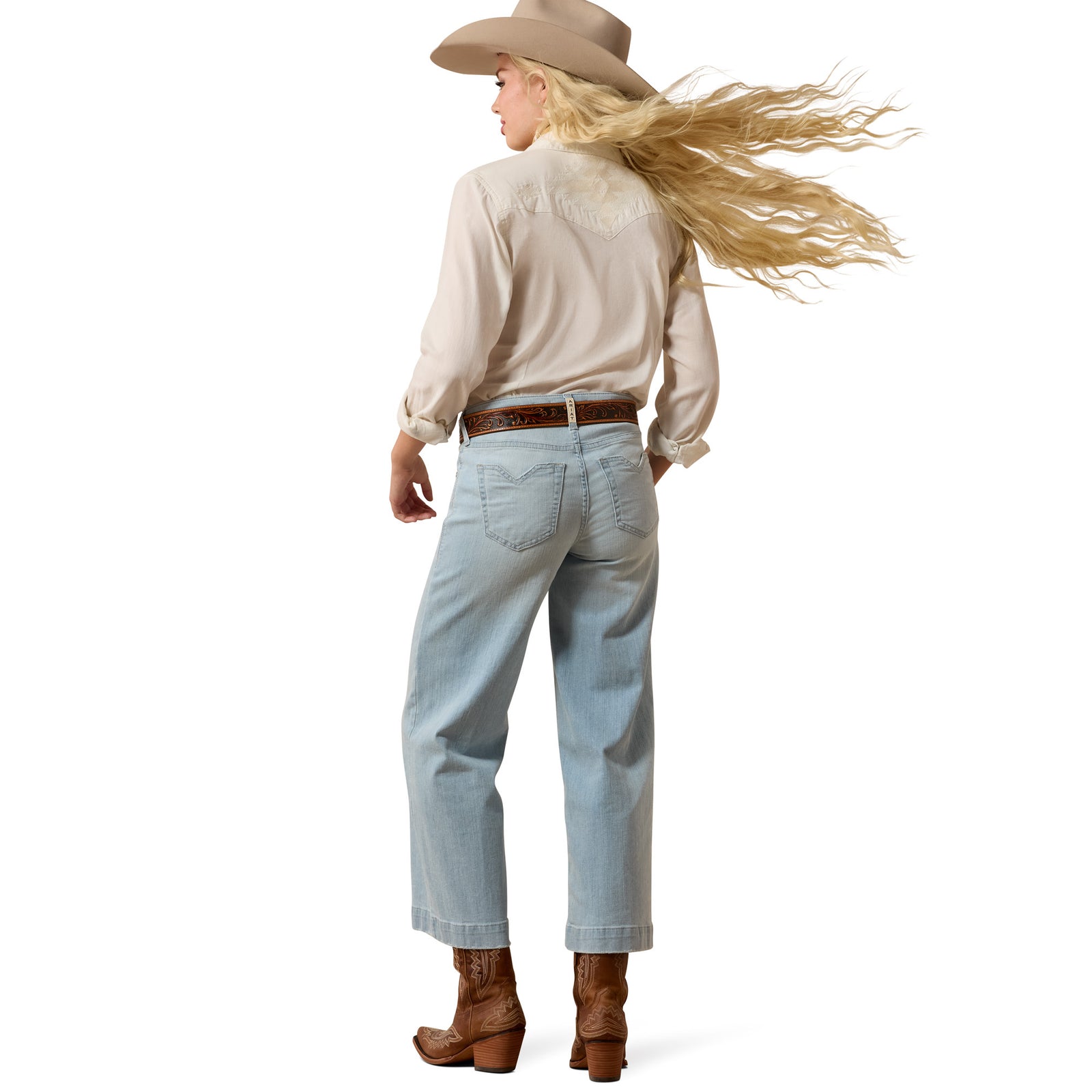Person wearing a beige shirt, light blue jeans, brown boots, and a beige cowboy hat on a white background