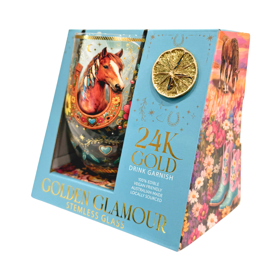 A boxed 24K gold drink garnish set in 'Golden Glamour' packaging, featuring a stainless steel stemless glass with a horse illustration and a lemon slice garnish inside a decorative blue and floral box.