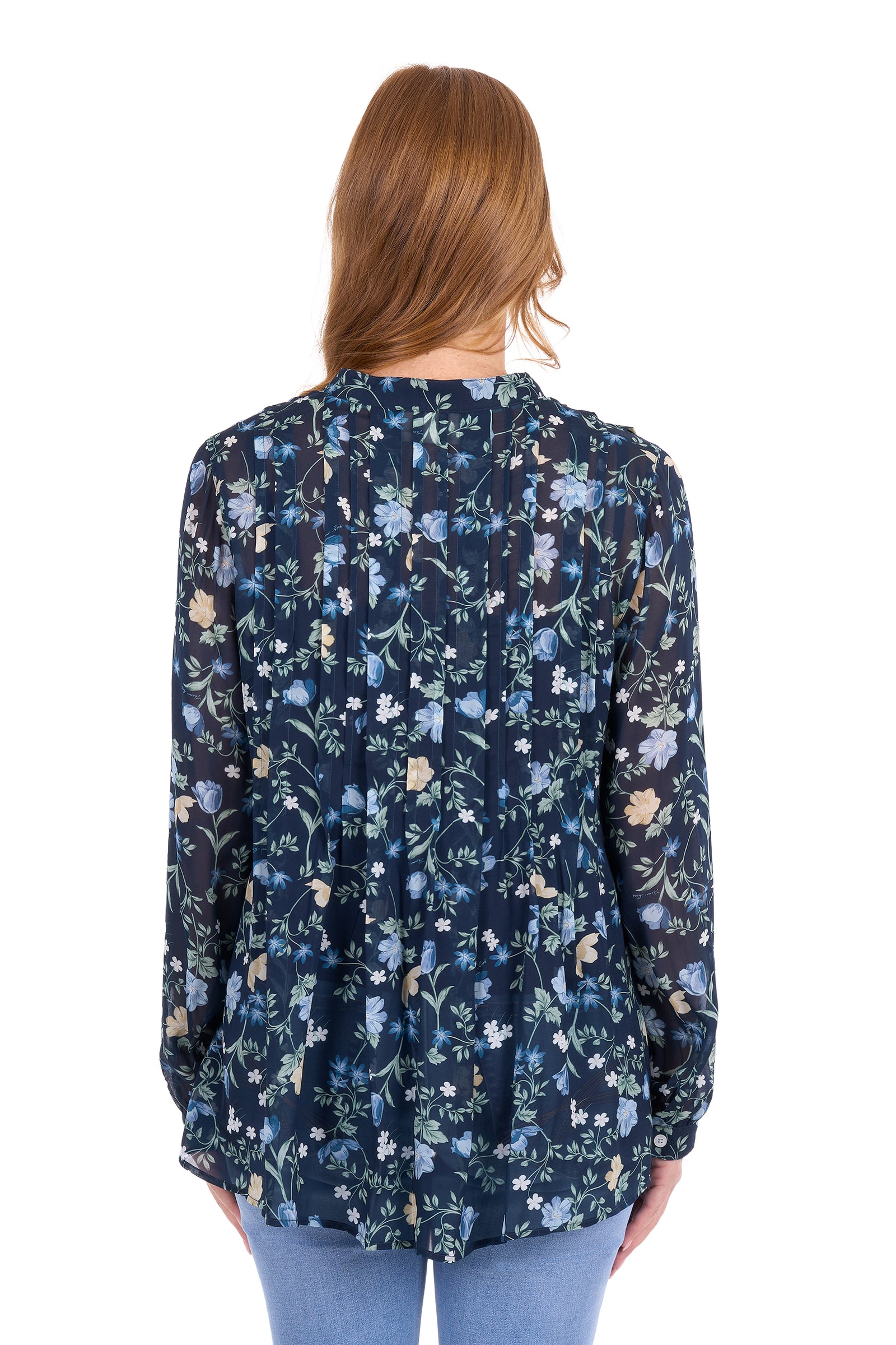 A woman viewed from the back wearing a long-sleeve navy blue blouse with a dense light blue, white, and beige floral pattern, paired with light blue jeans against a plain white background.