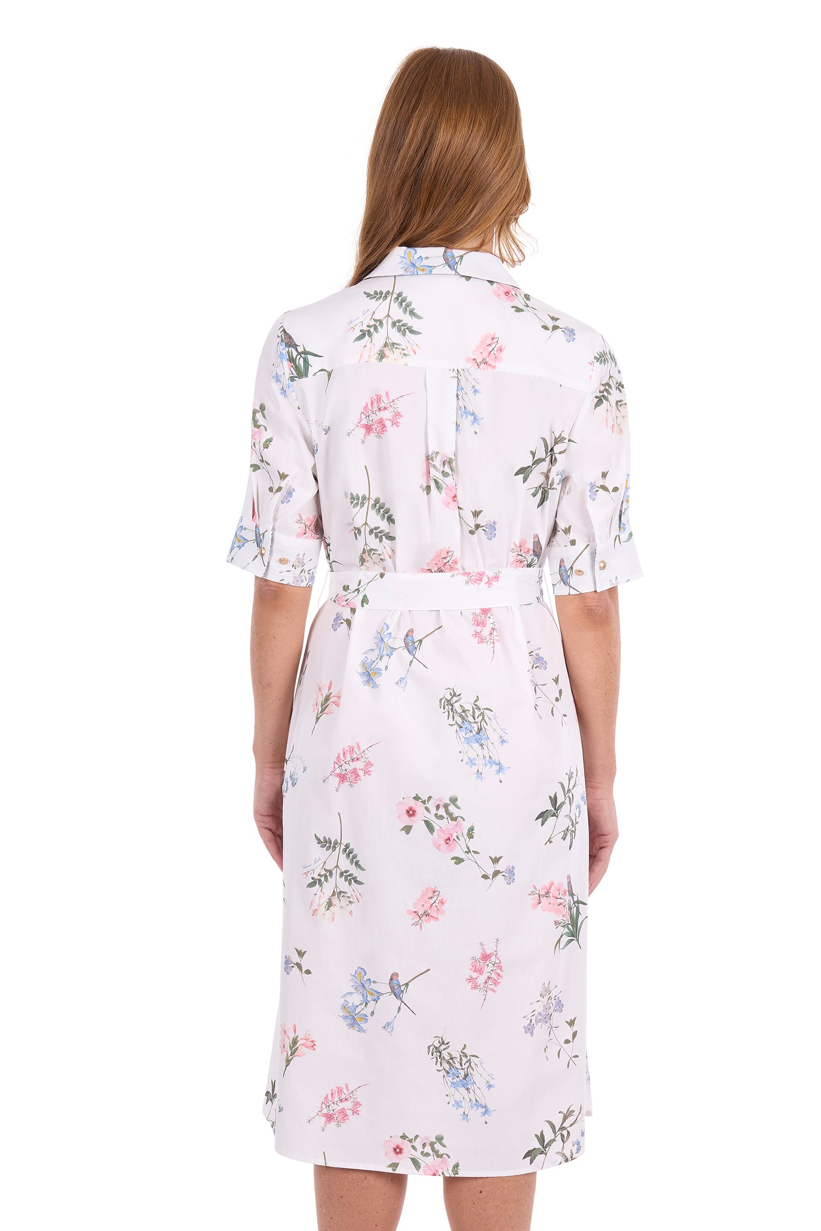 A woman viewed from the back wearing a short-sleeve collared dress with a white base and a delicate multicolor floral print in pink, blue, and green, set against a plain white background.