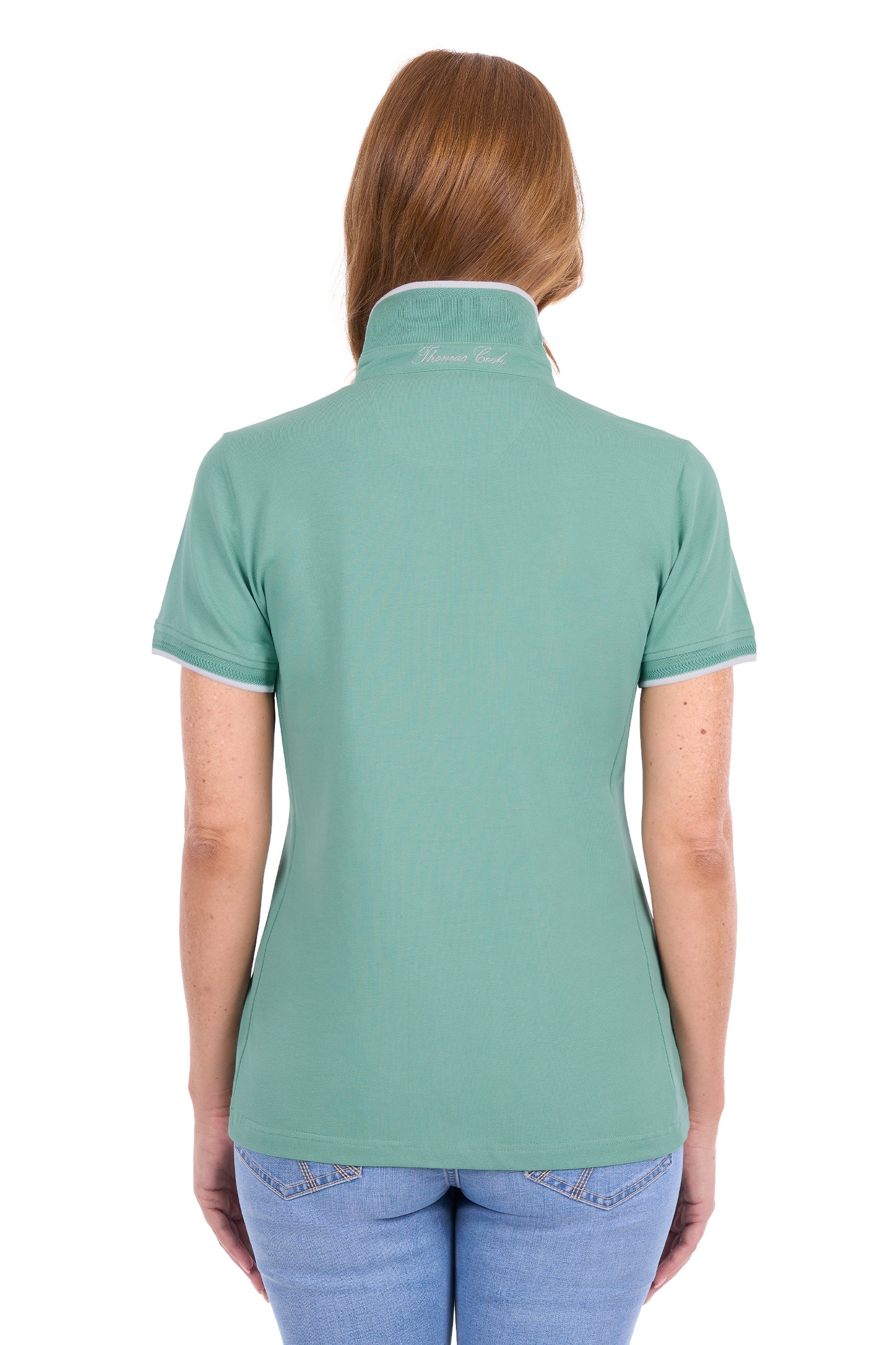 A woman viewed from the back wearing a sage green short-sleeve polo shirt with white trim on the collar and sleeve cuffs, paired with blue jeans against a plain white background.