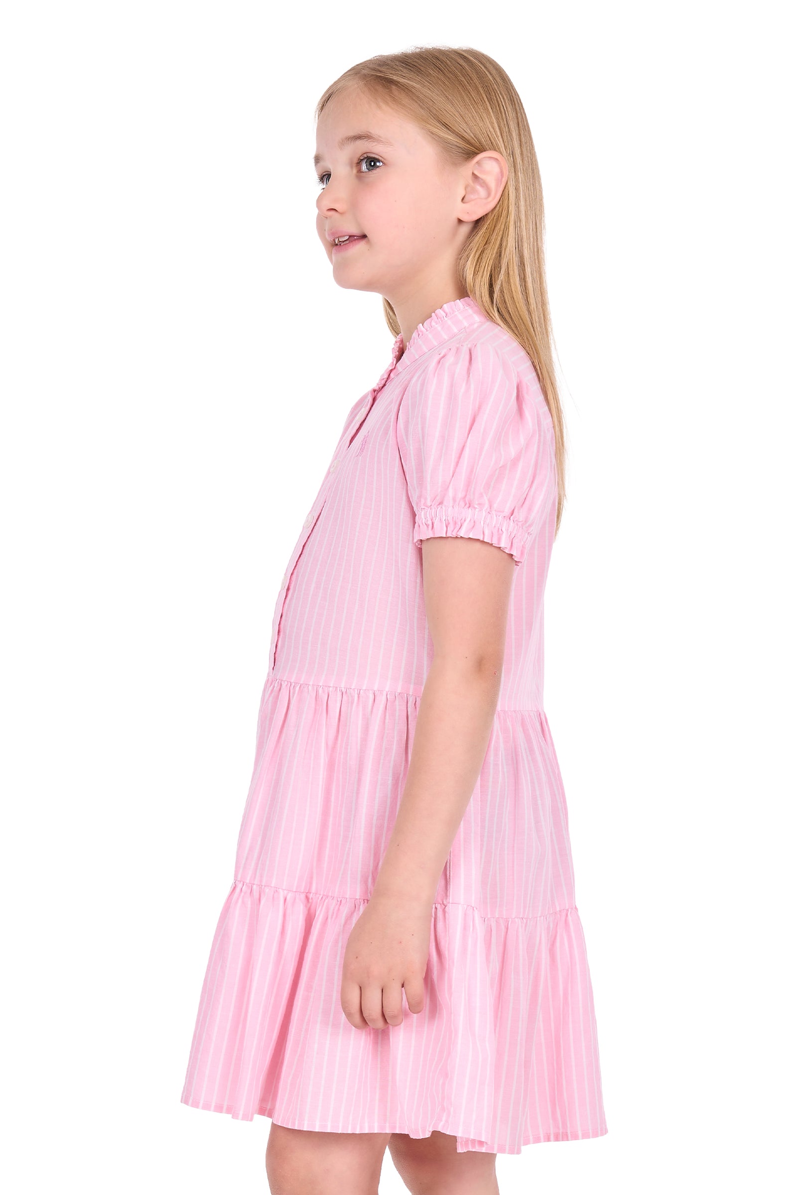 A young girl with blonde hair is shown from the side profile wearing a light pink tiered dress with vertical stripes, set against a plain white background.