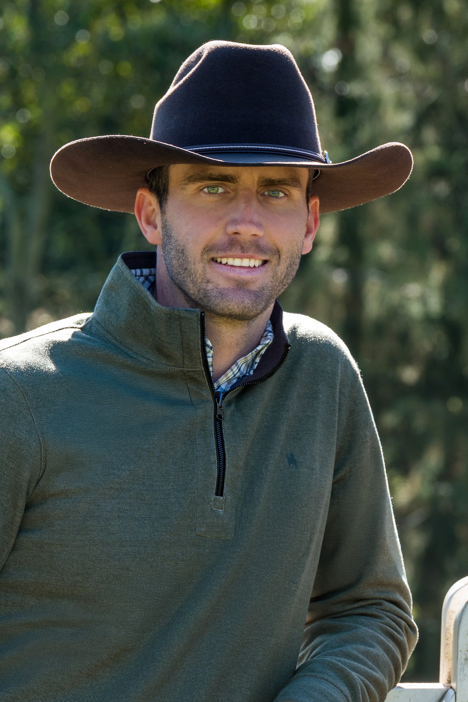 Man wearing a cowboy hat and green pullover with a blurred natural background
