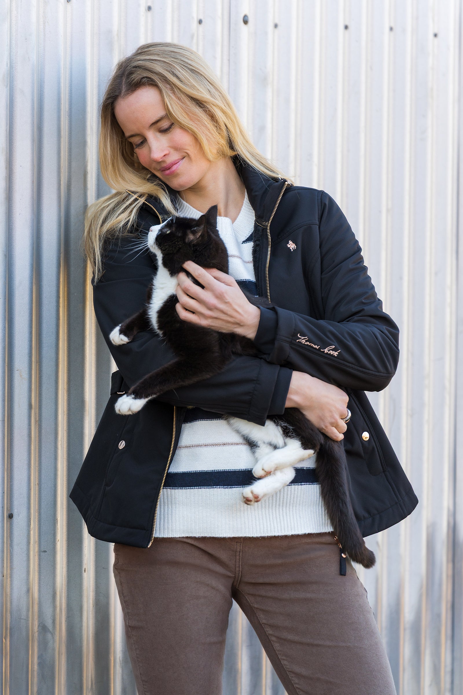 Woman holding a black and white cat against a metallic wall