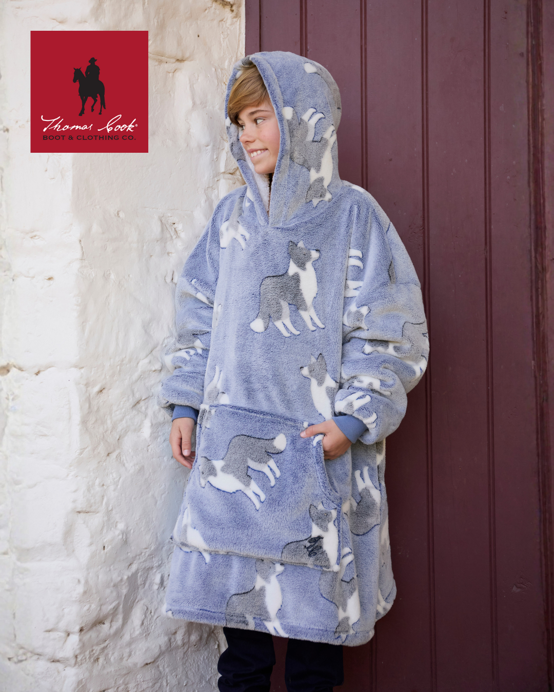 Child wearing a blue poncho with dog patterns against a textured wall and wooden door.