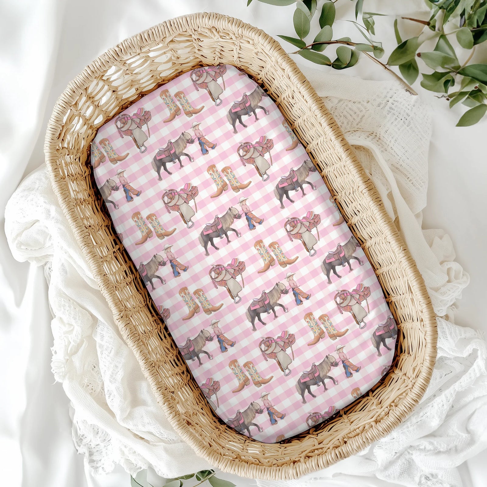 Wicker baby crib with pink and white striped sheet featuring animal patterns on a white background.