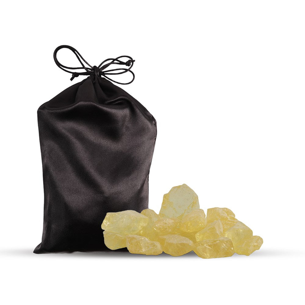 Rosin with Bag. A black satin bag tied with a ribbon bow, with amber rosin spilling out in front of it against a white background.