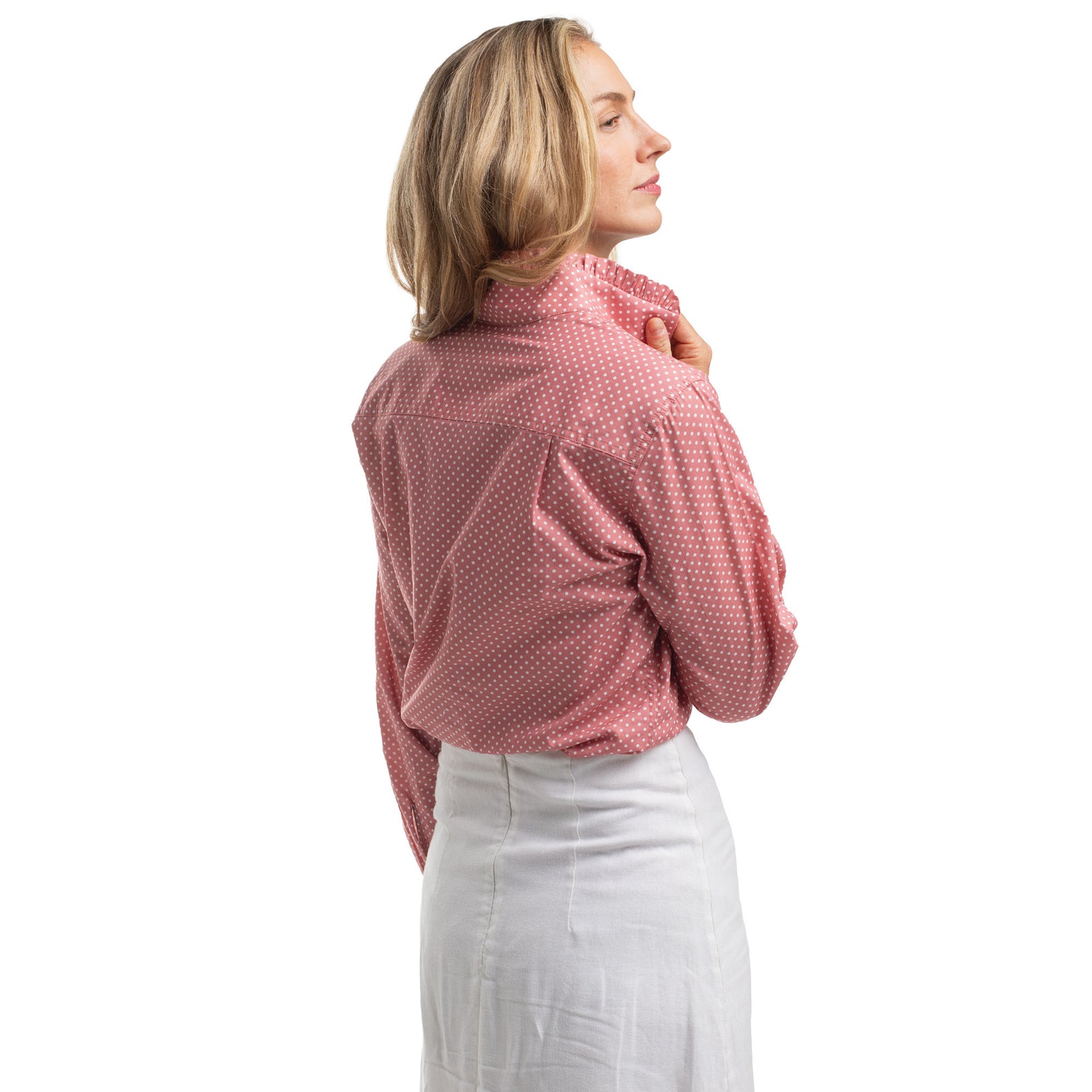 Woman wearing a pink polka dot blouse and white pants on a white background