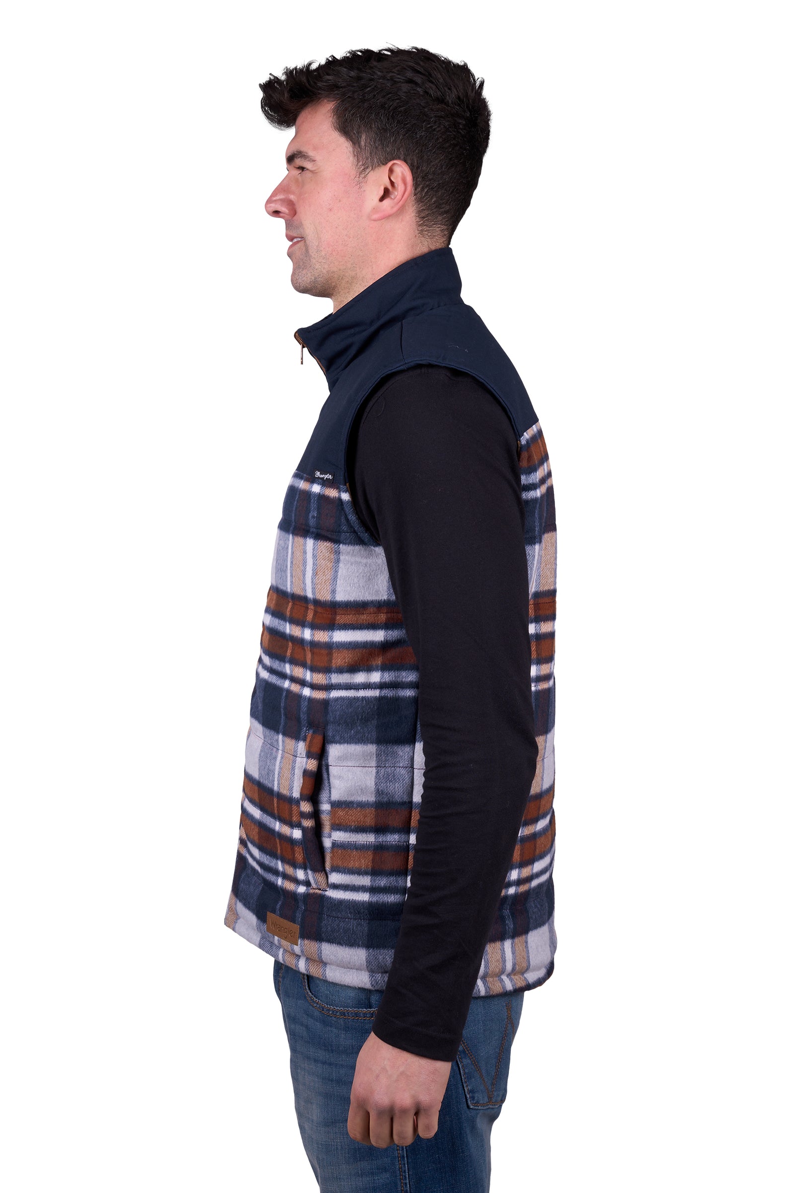 A man wearing a Wrangler Men's Koda Reversible Vest in navy and beige colors, paired with a black shirt and blue jeans.