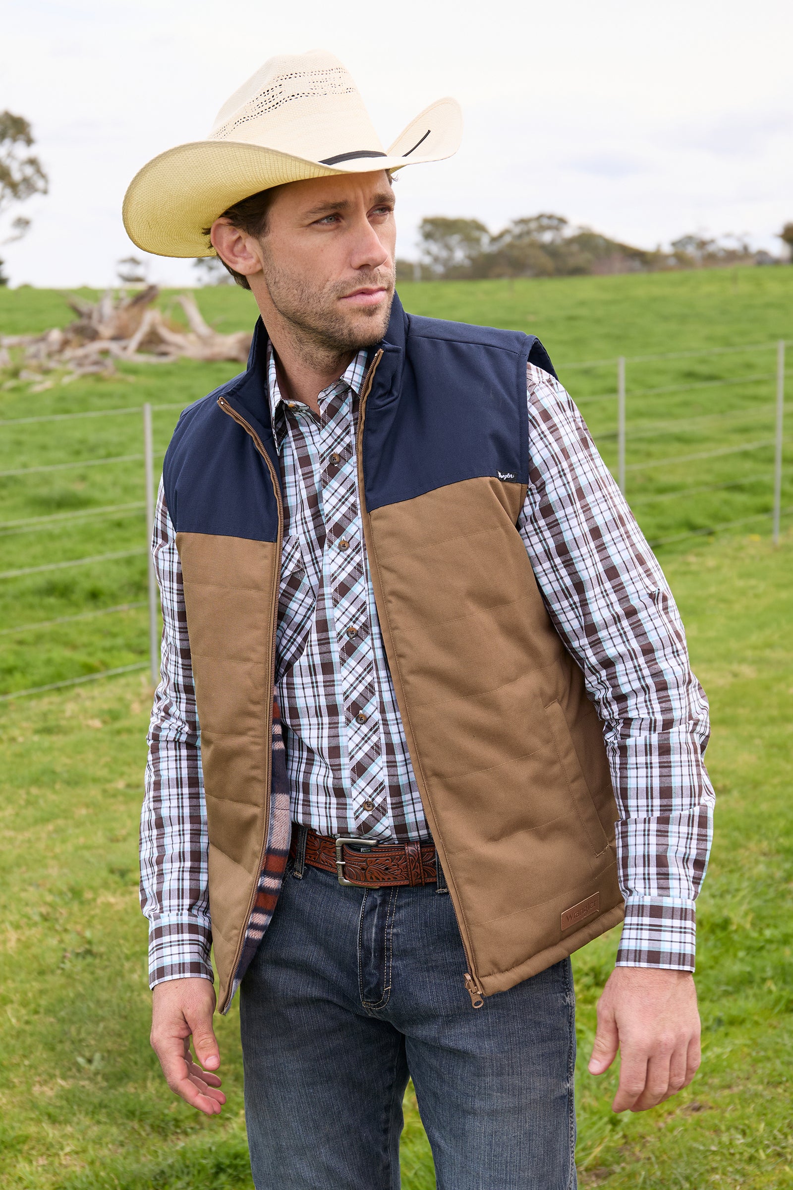 A man wearing a Wrangler Men's Koda Reversible Vest in navy and beige colors, paired with a black shirt and blue jeans.
