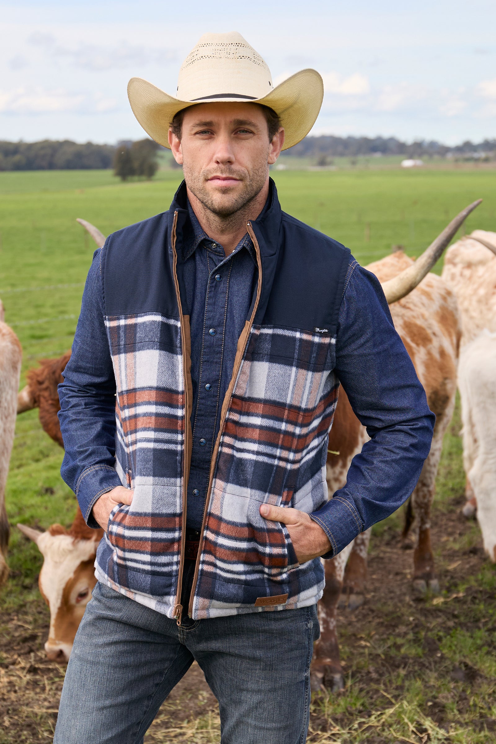 A man wearing a Wrangler Men's Koda Reversible Vest in navy and beige colors, paired with a black shirt and blue jeans.