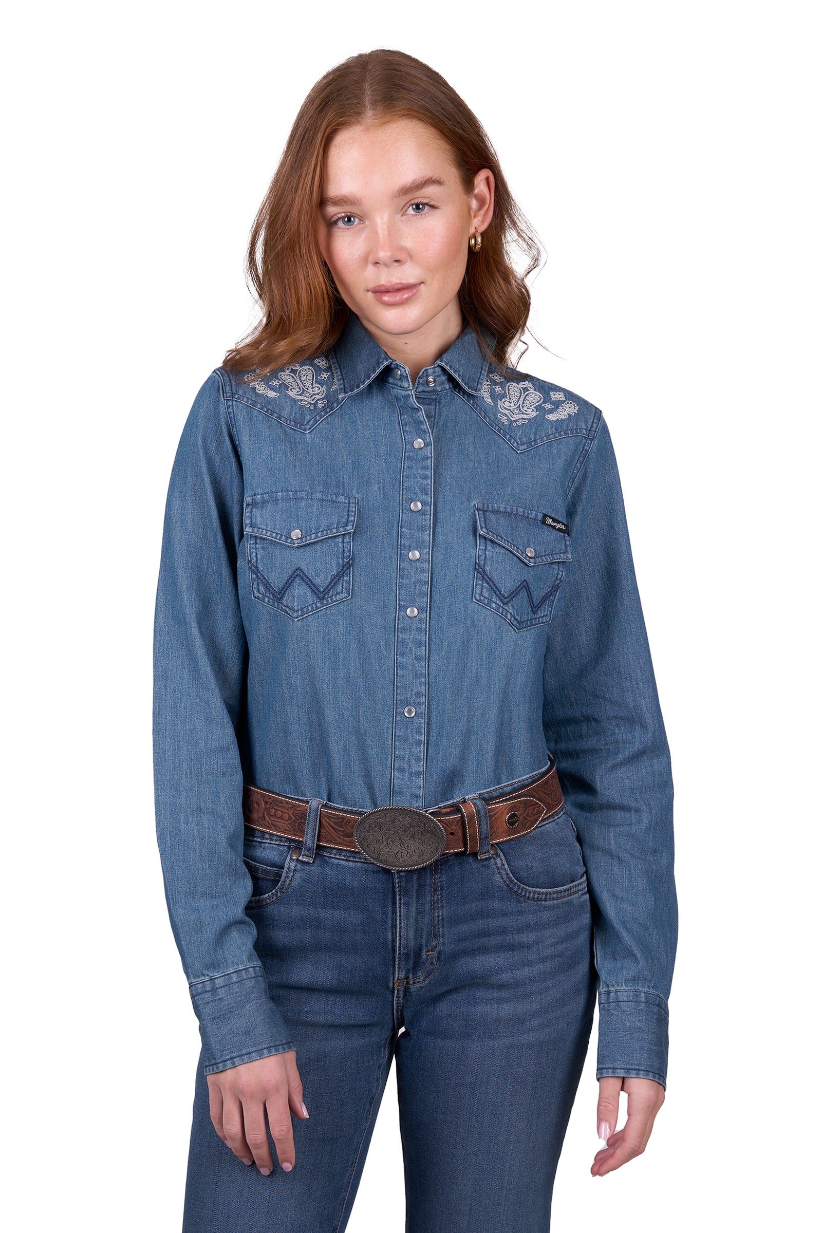 A woman wearing a wrangler western embroidered demim western shirt with paired with blue jeans.