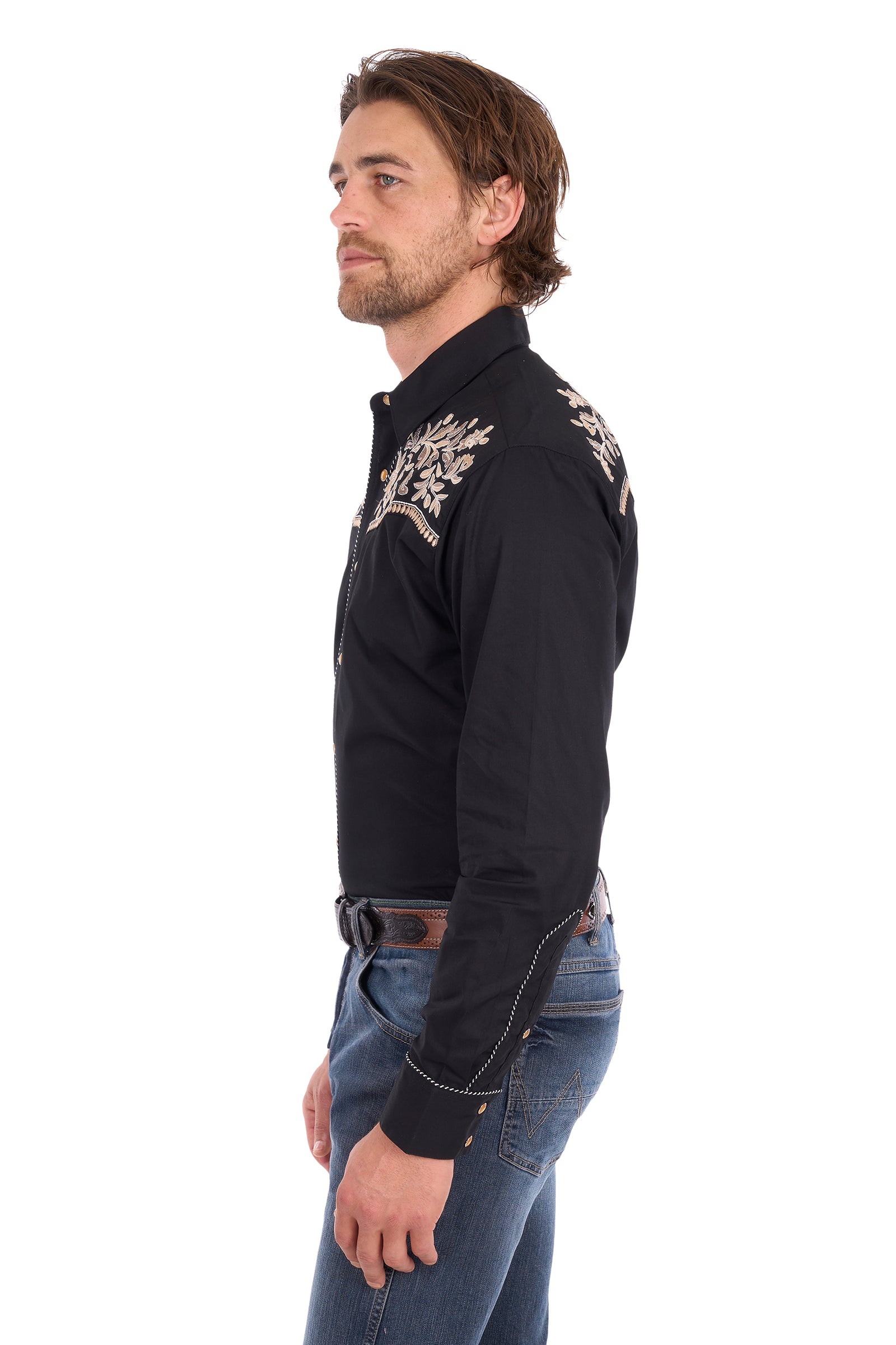 A man shown in profile wearing a black long-sleeve western shirt with ornate silver embroidery on the shoulders and upper chest, paired with blue jeans, against a plain white background.
