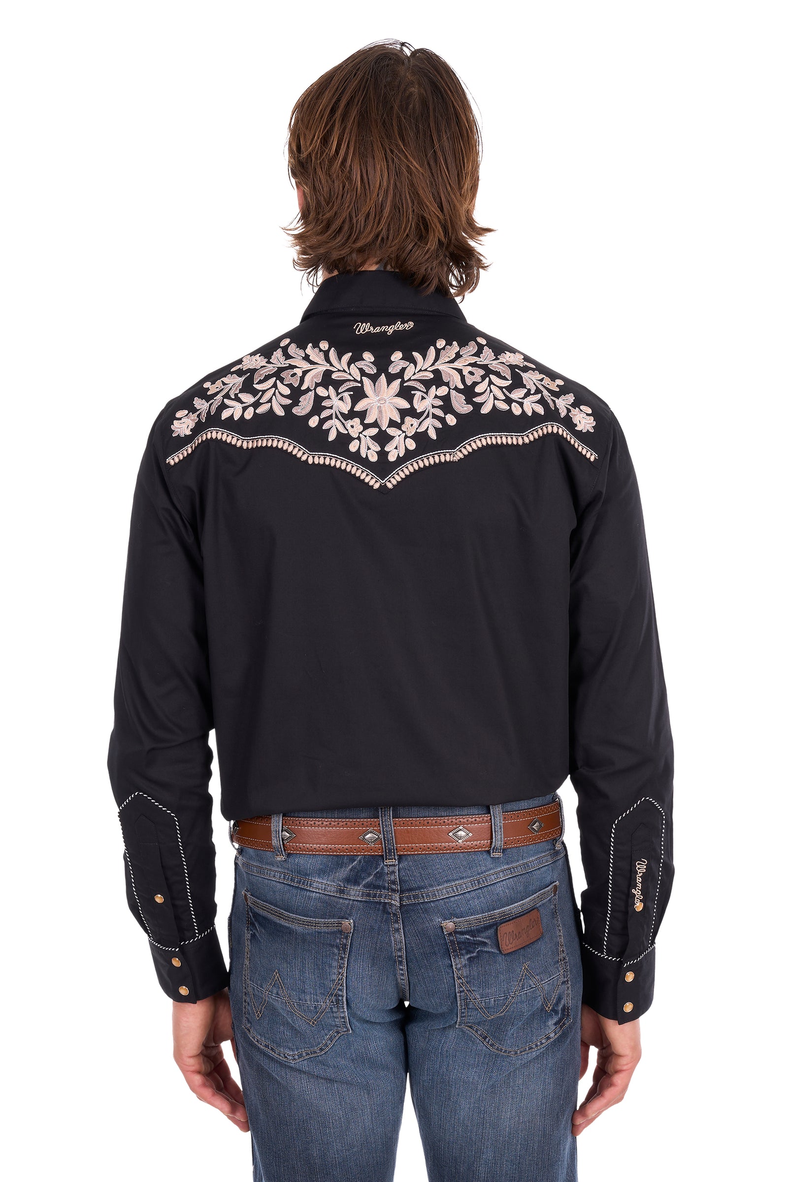 Rear view of a man wearing a black Wrangler western shirt with intricate white embroidery across the shoulders and upper back, paired with blue jeans and a brown belt, on a white background.