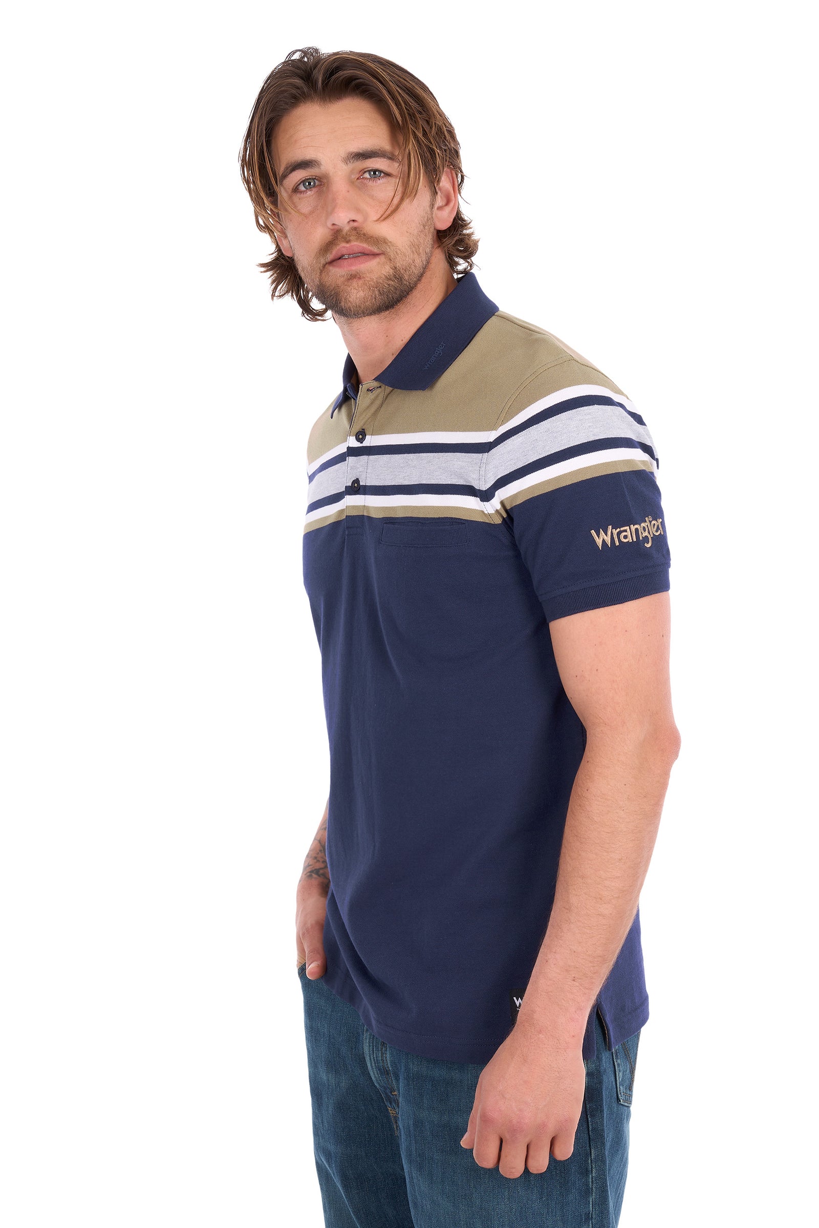 A man wearing a Wrangler short-sleeve polo shirt in navy blue with beige and white stripes across the chest and shoulders, paired with blue jeans, photographed against a plain white background.