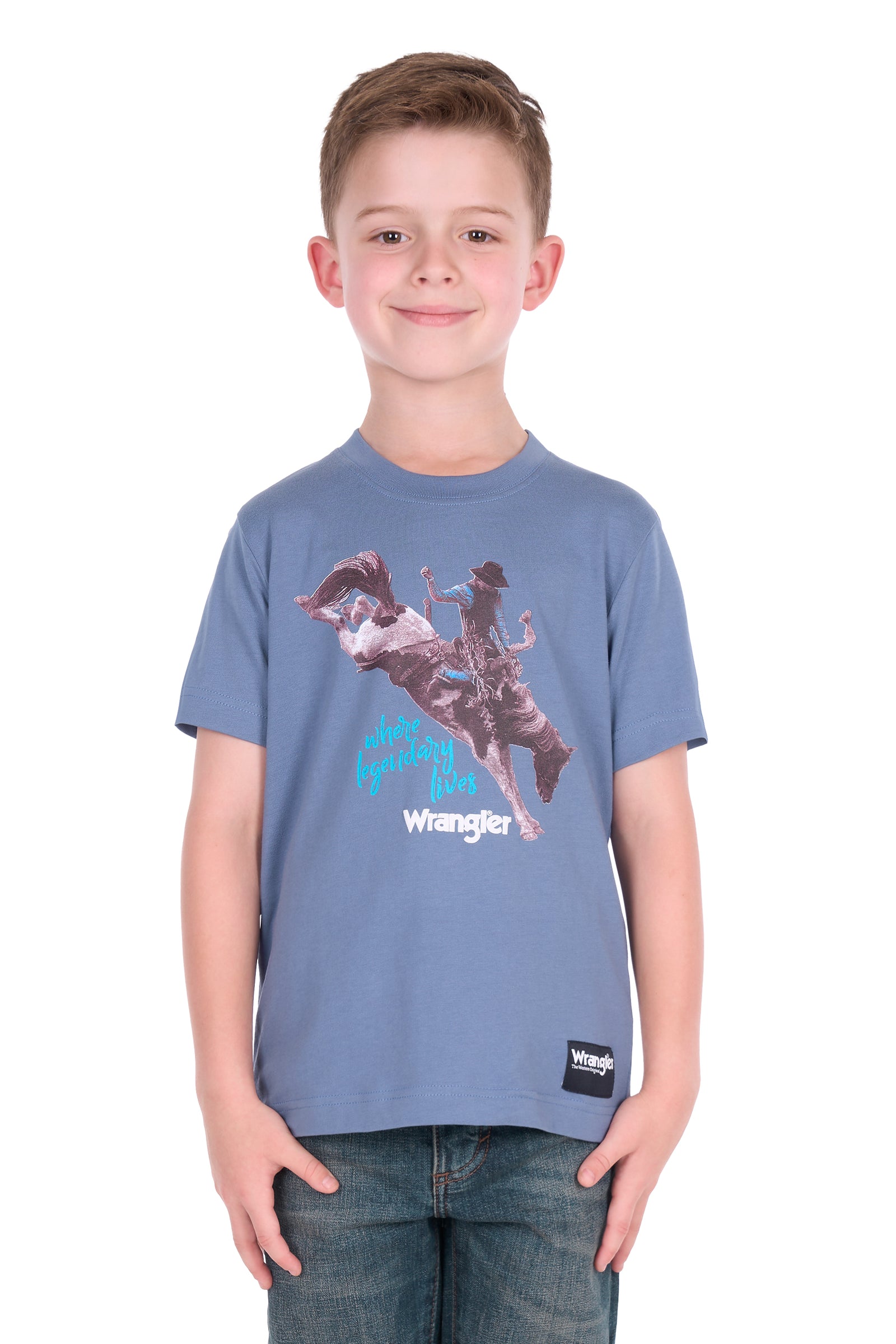 A young boy wearing a blue Wrangler t-shirt with a cowboy graphic print, paired with blue jeans, standing against a plain white background.