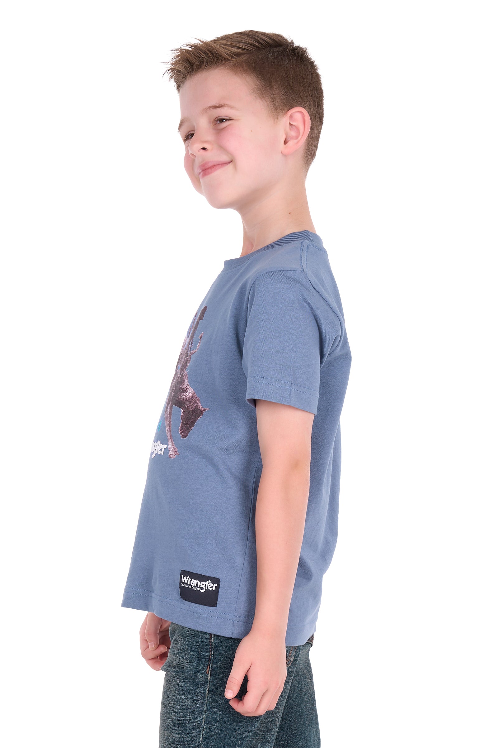 A young boy shown from the side profile wearing a blue Wrangler short-sleeve t-shirt and dark blue jeans, photographed against a solid white background.