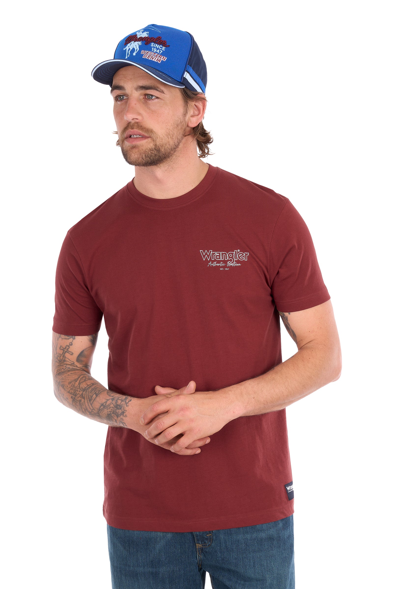 A man wearing a maroon Wrangler short-sleeve t-shirt and a blue trucker hat, standing against a white background.