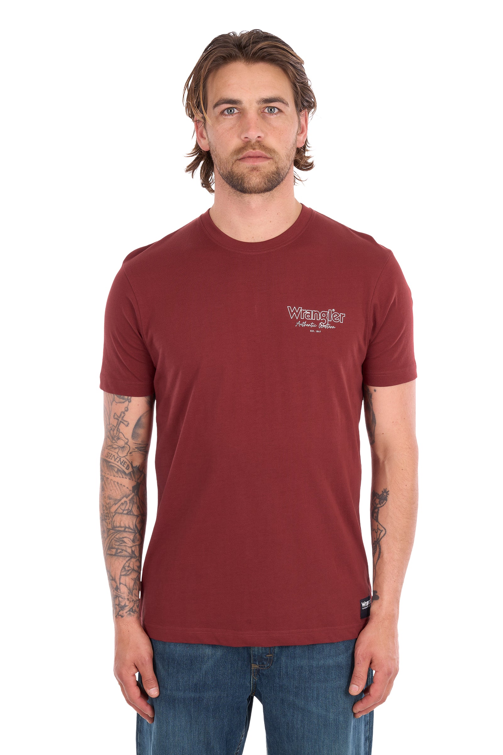 A man wearing a maroon crew-neck t-shirt with a small white graphic on the left chest, paired with blue jeans, photographed against a plain white background.