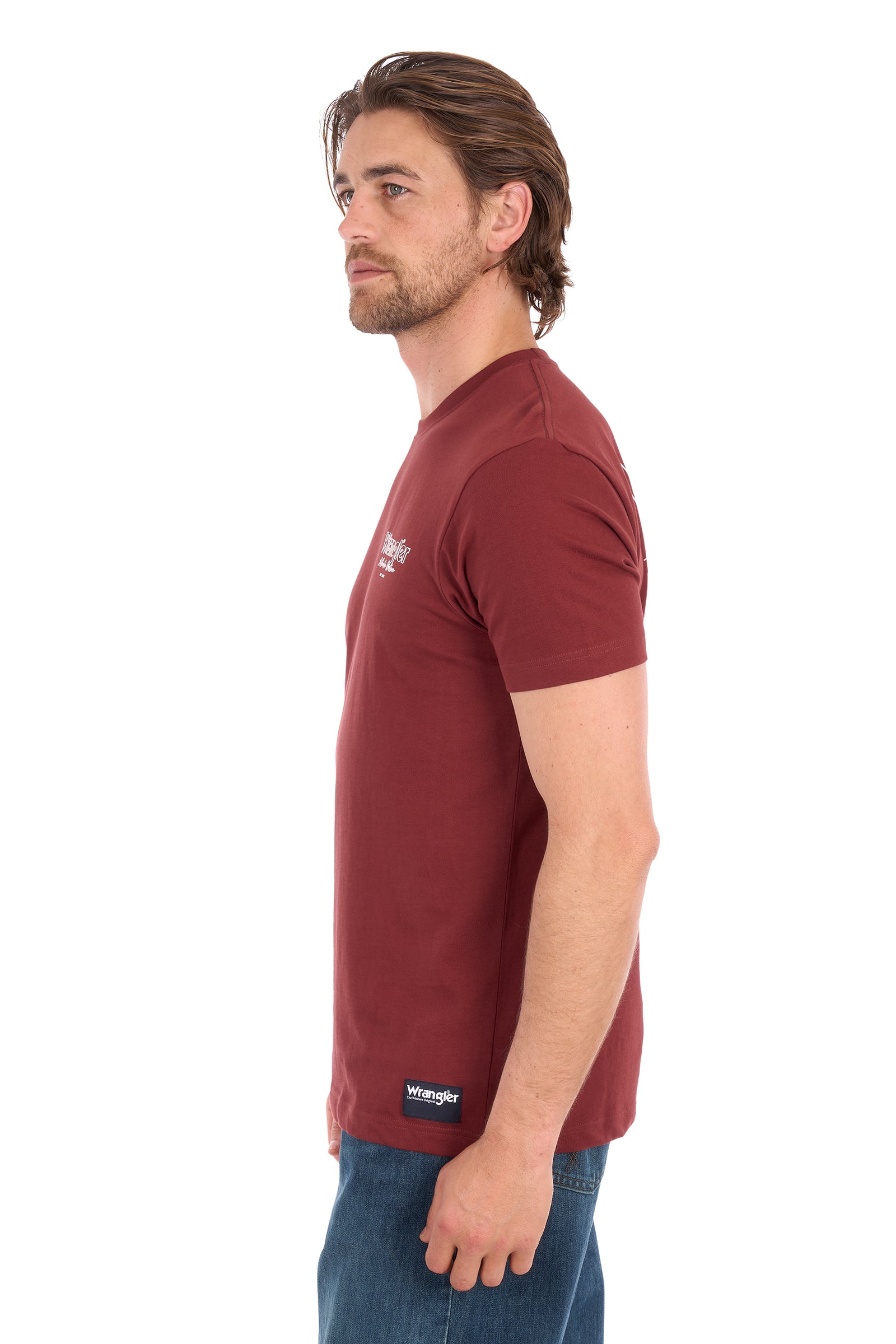 A man shown in profile wearing a maroon short-sleeve crewneck t-shirt with a small white chest logo and a black brand label near the hem, paired with blue jeans against a plain white background.