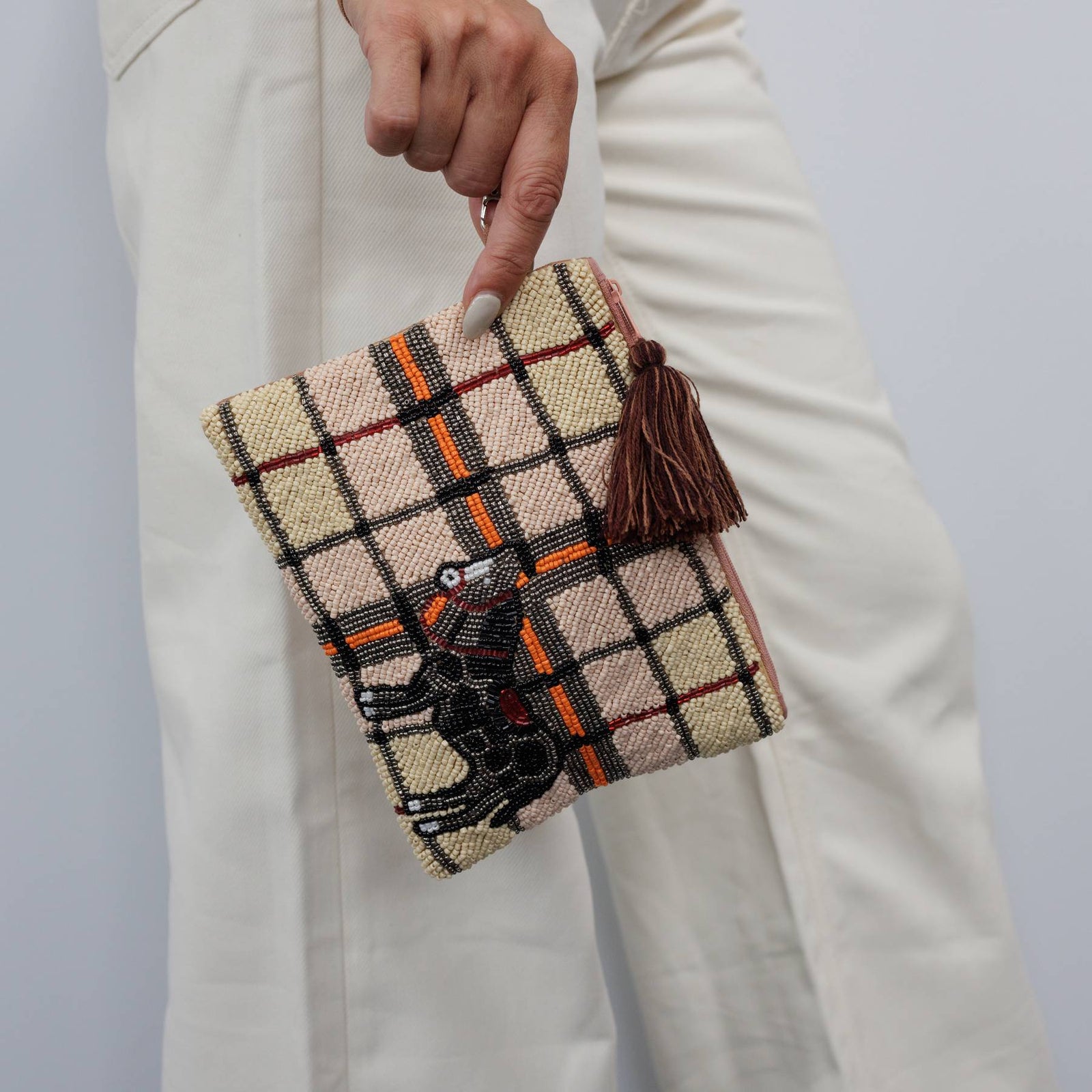 Hand holding a plaid clutch with tassel and embroidered design against a plain background
