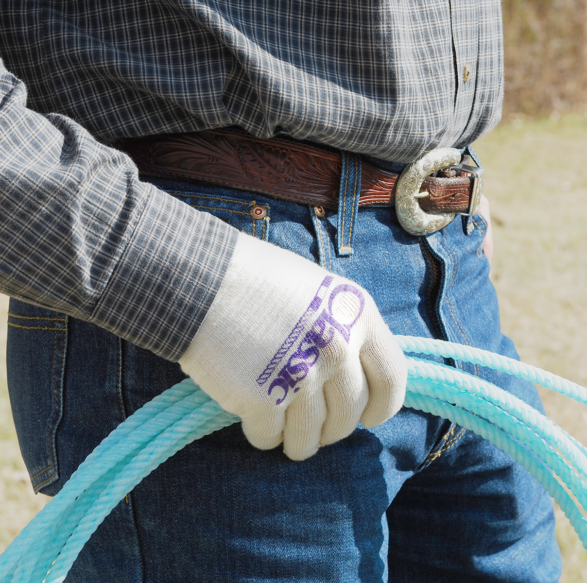 Classic Deluxe Roping Glove 12 Pack. A person wearing a gray synthetic blend hi-tech fibres glove with the brand name 'Classic' written on it, holding a blue rope.