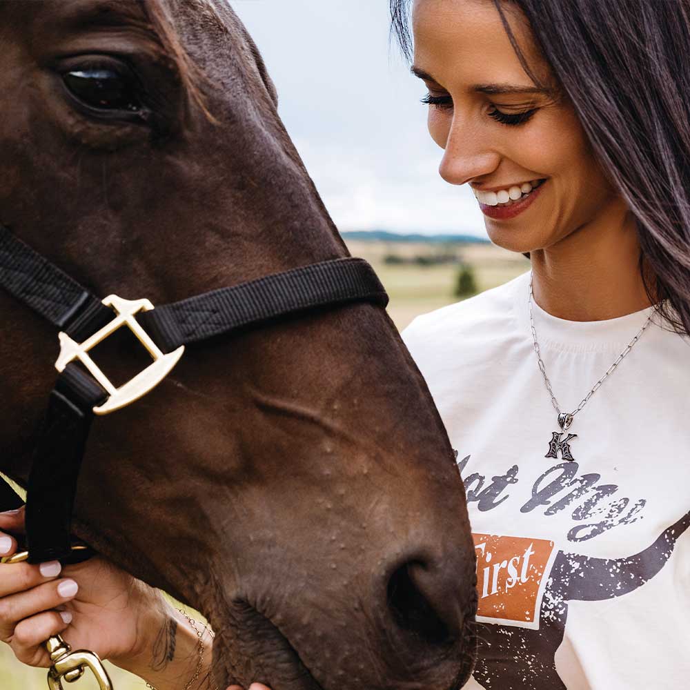 Montana Silversmiths Western Initials Necklace. Woman smiling and petting a horse with a scenic background