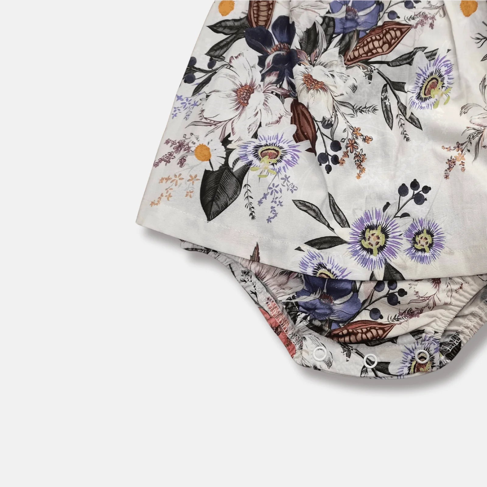 A folded pair of white shorts featuring a detailed botanical and floral print with purple, blue, green, and orange elements, shown on a clean white background.