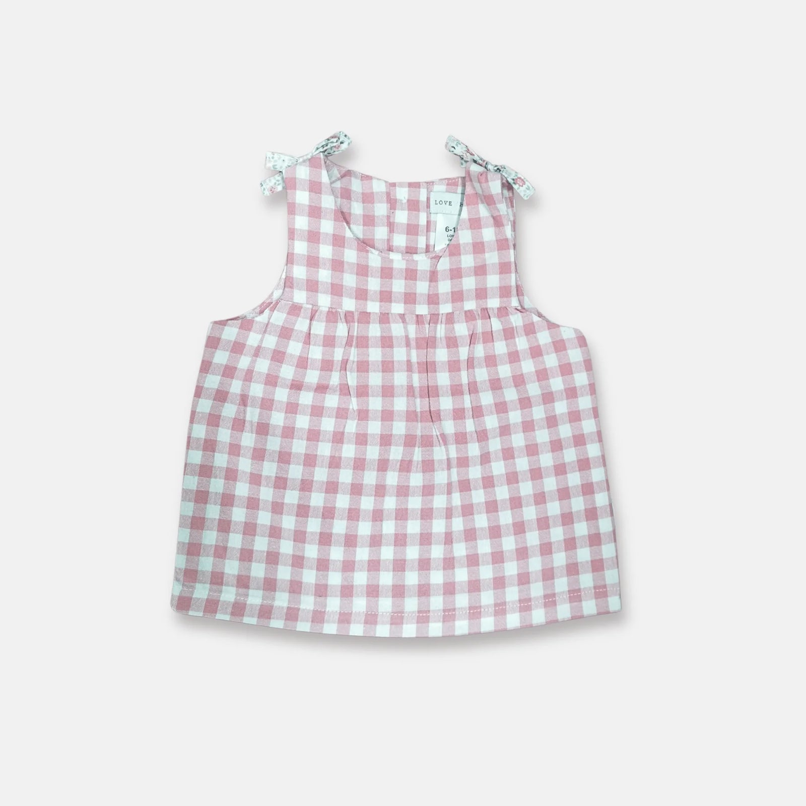 A sleeveless baby dress with a pink and white gingham check pattern, featuring tie-shoulder straps with a light green floral print, shown flat on a light gray background.