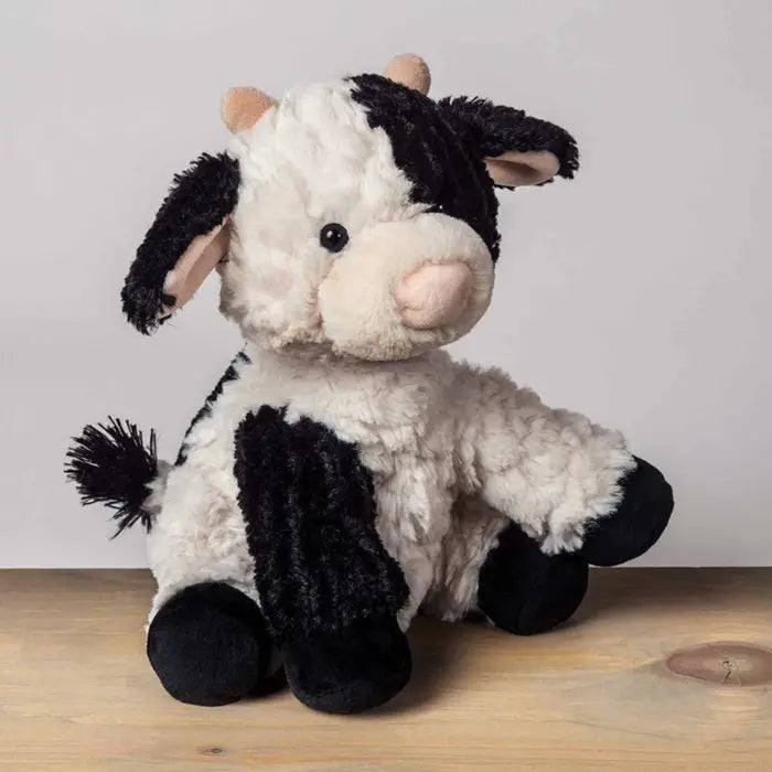 Plush cow toy on a wooden surface with a light gray background