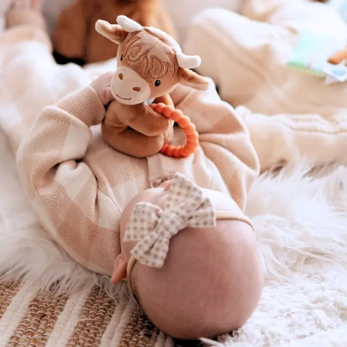 Baby wearing a pink outfit with a soft toy on a fluffy white blanket