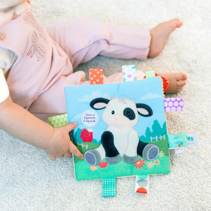 Child holding a soft book with a cow illustration on a carpeted floor