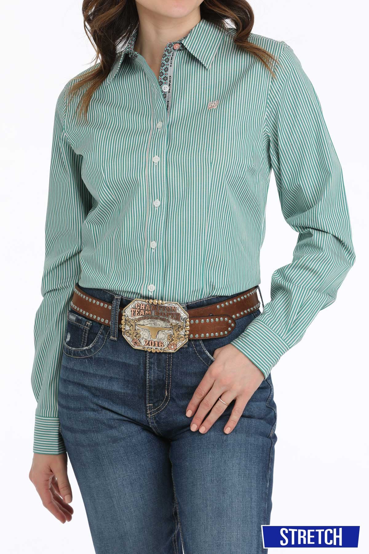Cinch Women's Stripe Button-Down L/S Western Shirt. Woman wearing a green striped shirt and blue jeans with a belt and buckle.