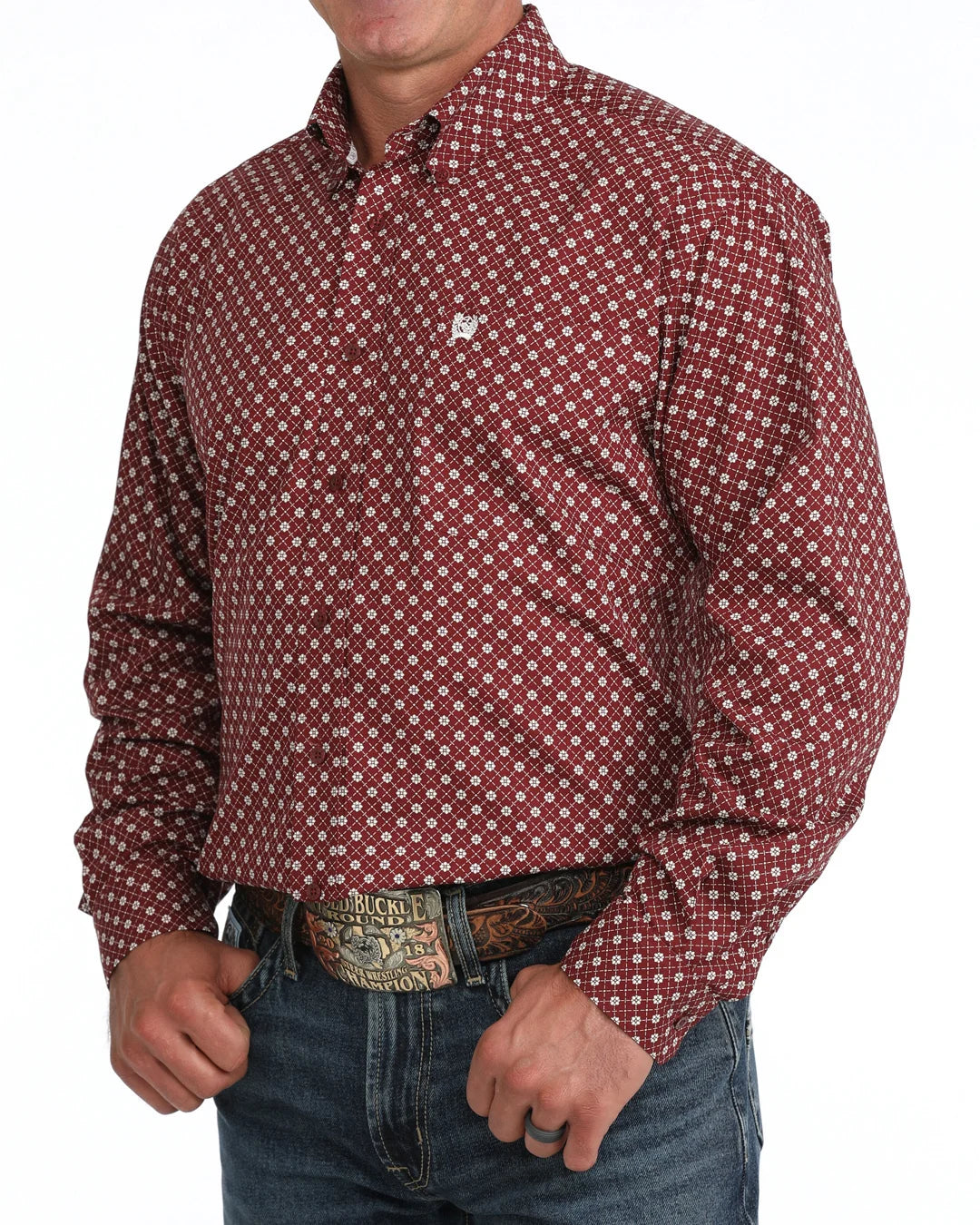 A man wearing a long-sleeve button-down shirt with a red and white geometric pattern, paired with blue jeans and a western belt.