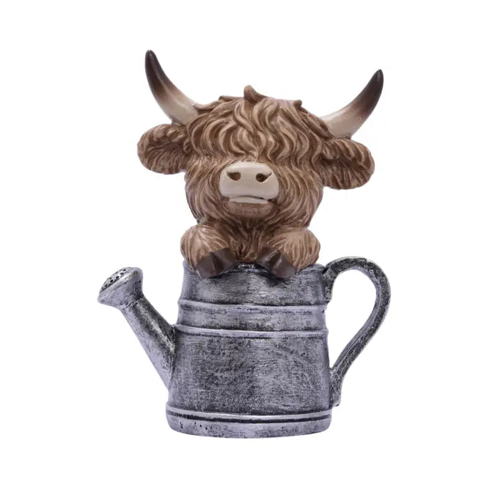 A decorative figurine of a brown highland cow with horns sitting inside a distressed gray metal watering can, isolated on a white background.