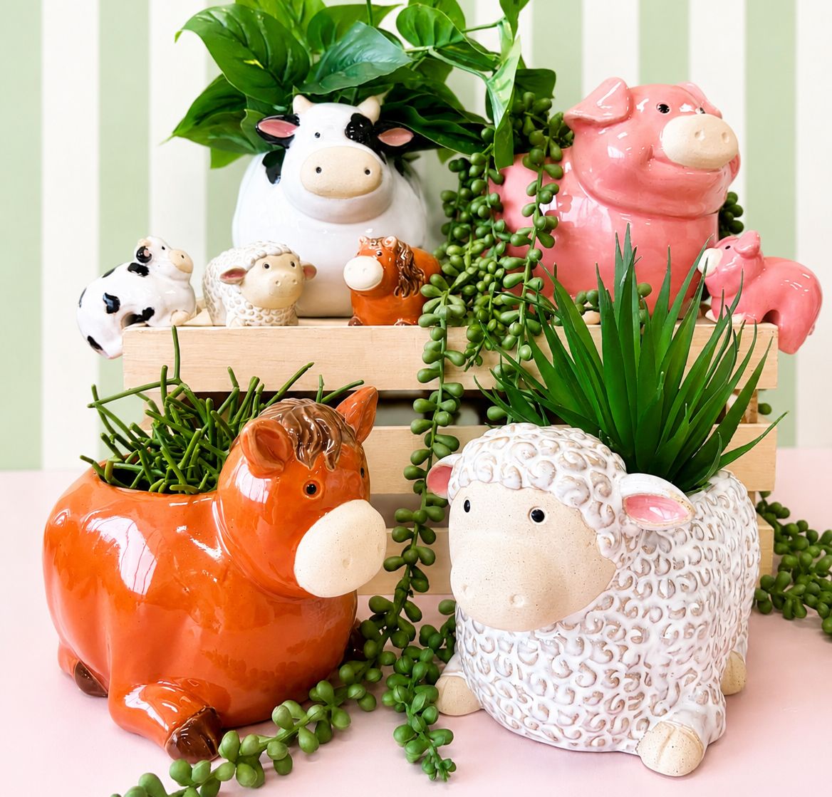 A collection of ceramic farm animal planters including an orange horse, a white sheep, a pink pig, and a black-and-white cow, arranged on a pink surface with green trailing plants against a light green and white striped background.